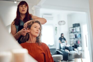 Mirror reflection of senior woman, hairdresser and salon studio employee working on client haircut, hair care or treatment. Designer hair salon, beauty spa service and stylist work on customer hair