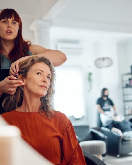 Mirror reflection of senior woman, hairdresser and salon studio employee working on client haircut, hair care or treatment. Designer hair salon, beauty spa service and stylist work on customer hair