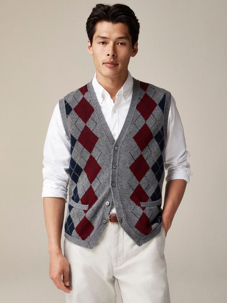 man from the waist up wearing a grey argyle sweater vest over a white button-down shirt and off-whtie pants