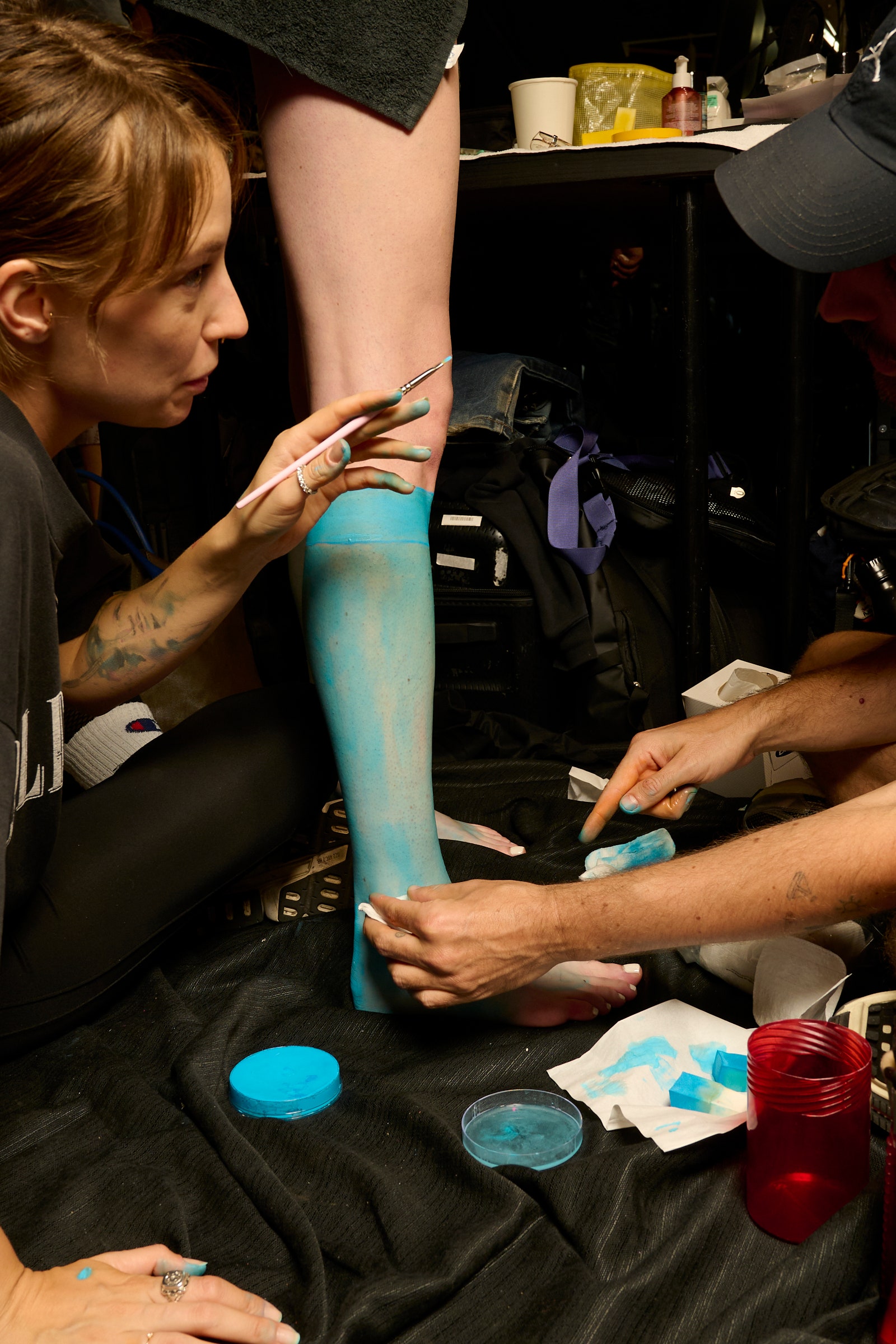 Makeup artists apply fake blue stockings to model's legs