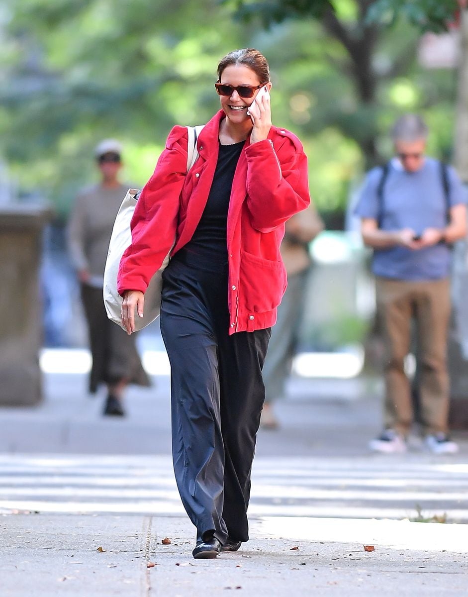 Katie Holmes is all smiles as she steps out in New York City. The American actress carries a large canvas tote and wears a red jacket, black blouse, matching trousers, and ballet flats