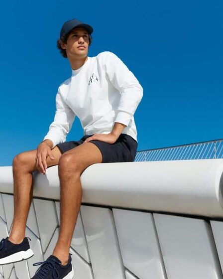 man in sweater and shorts sitting on a concrete fence