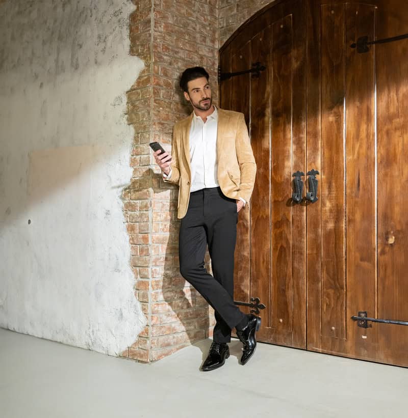 man standing cross-legged and shoulder leaning to a wall