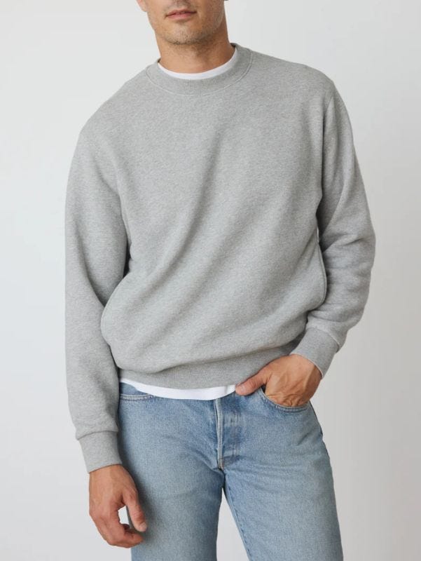 man from the neck to the waist wearing a grey crewneck sweatshirt over a white t-shirt with light blue jeans