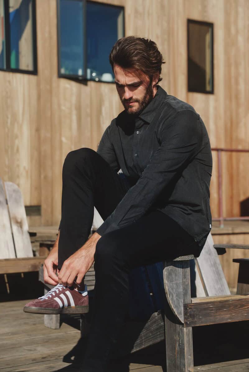 man sitting on the arm of a chair while tying a shoelace