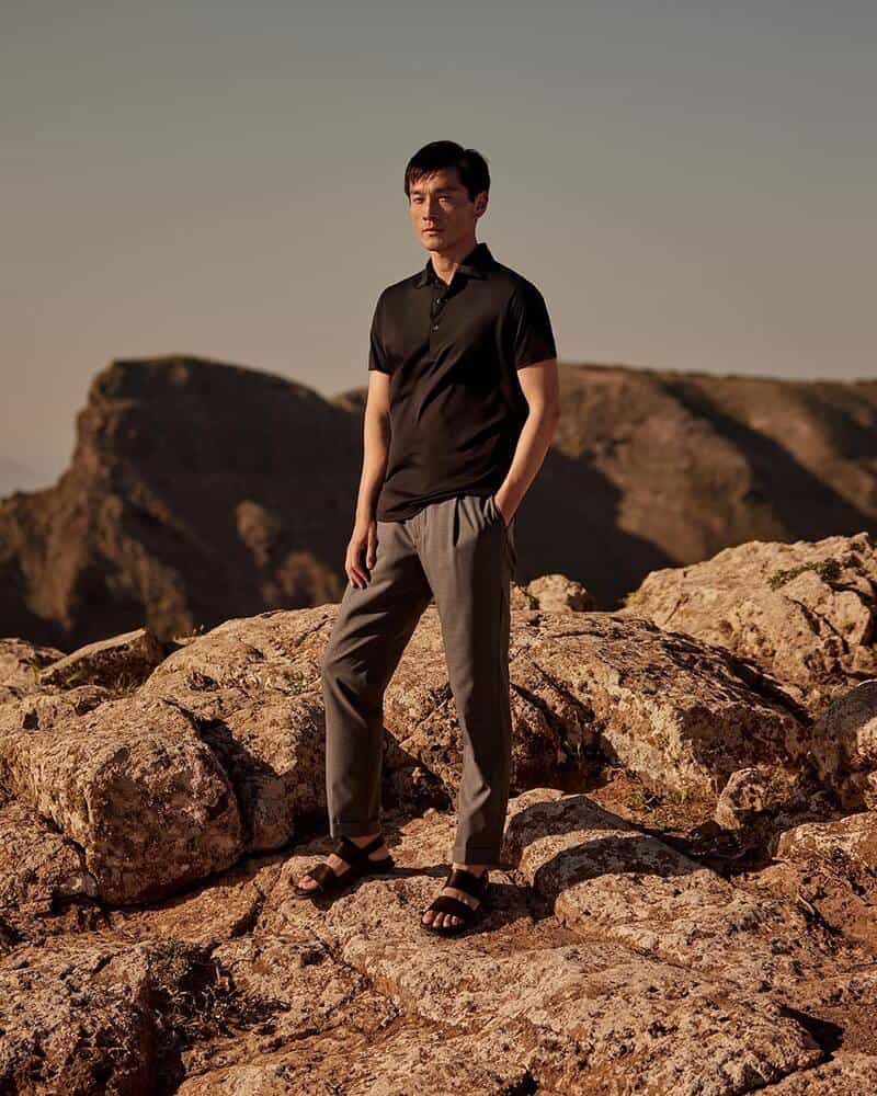 man standing on rocky cliff wearing lightweight trousers by luca faloni