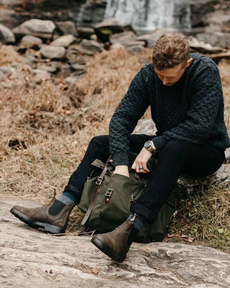 man sitting on a rock while checking the pocket of a backpack