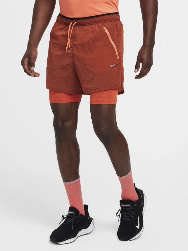 lower half of a man wearing orange running shorts, orange socks, and black running sneakers