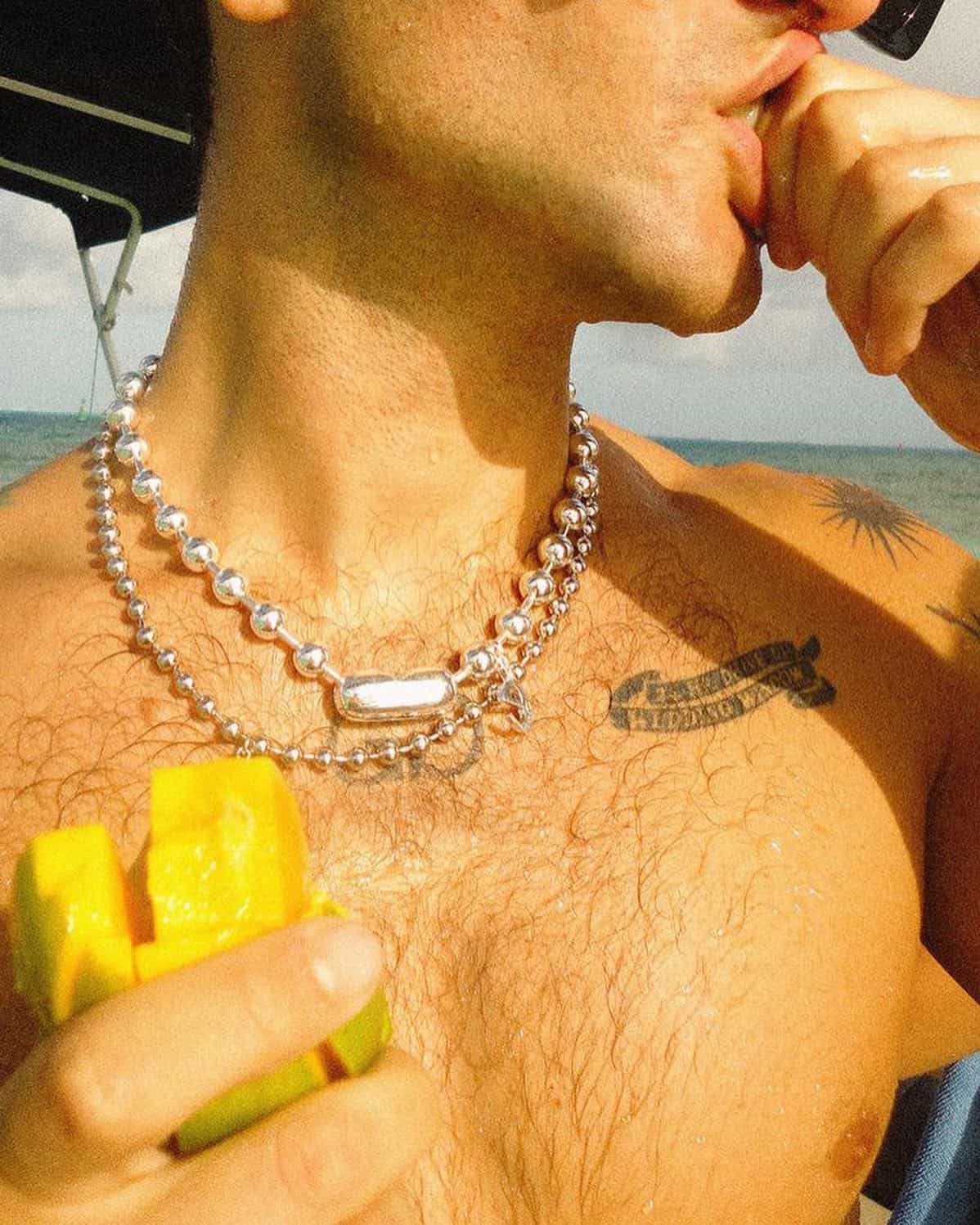 man wearing a pair of silver necklace and eating a mango