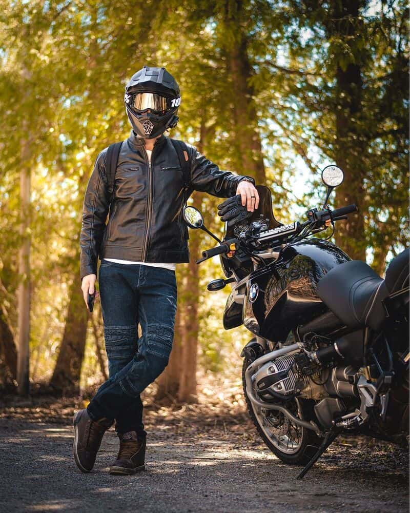 man standing beside a motorcycle wearing a racer leather jacket by decrum