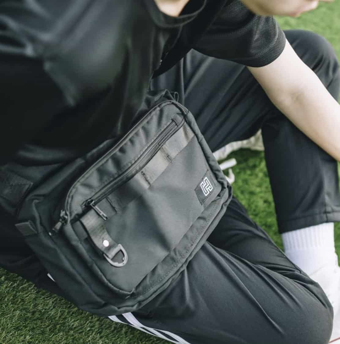 man sitting on grass with sling bag