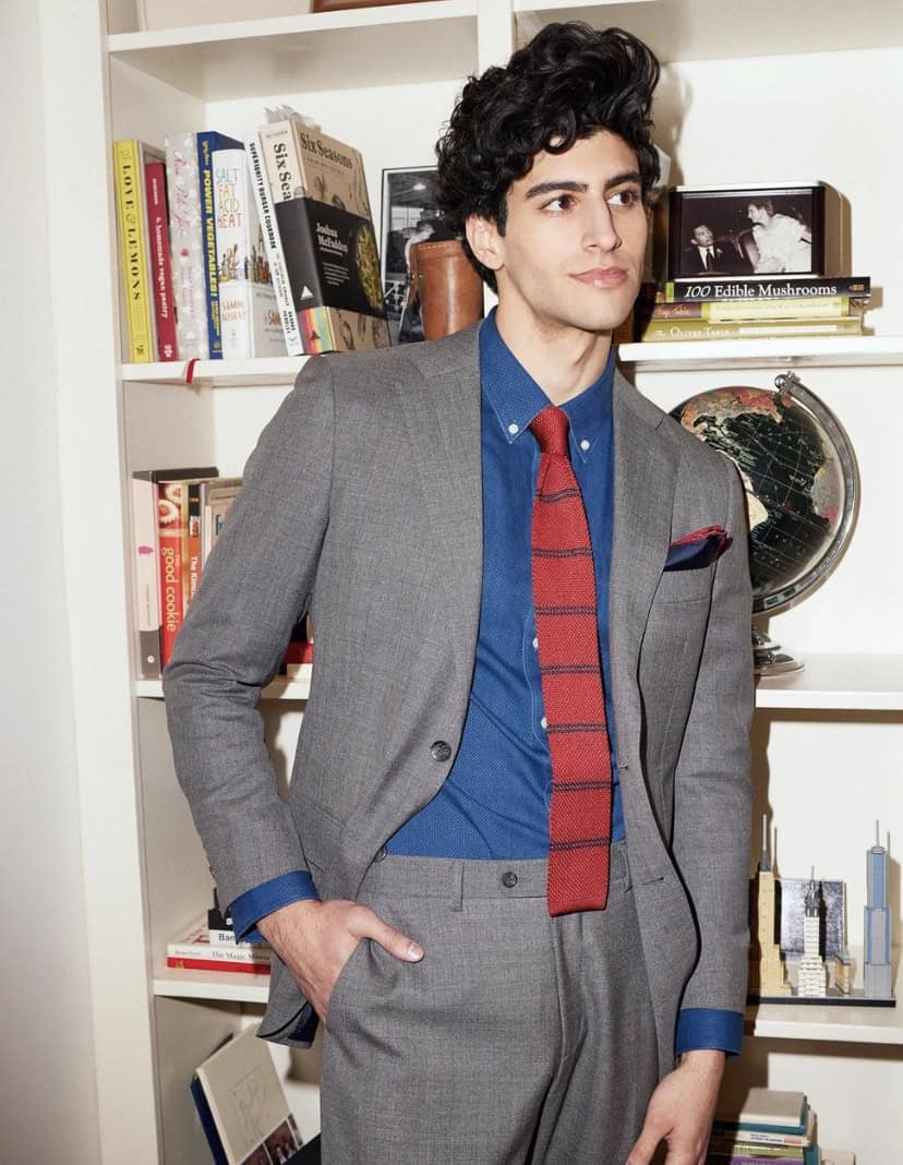 Man wearing a suit with his hand in his pocket, standing in front of a bookcase