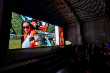 A dark room with an audience and a big screen with a fashion campaign image with "strengthening brand positioning" on the screen.