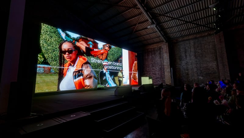 A dark room with an audience and a big screen with a fashion campaign image with "strengthening brand positioning" on the screen.