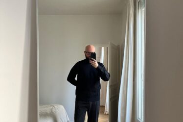 man at home taking a selfie in a full length mirror wearing all black