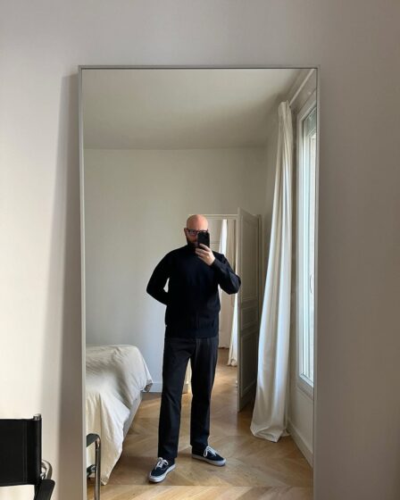 man at home taking a selfie in a full length mirror wearing all black