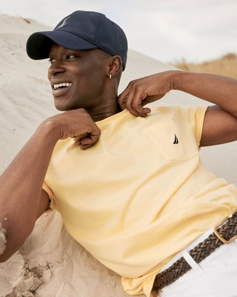 A man lying on the sand wearing a nautica t-shirt