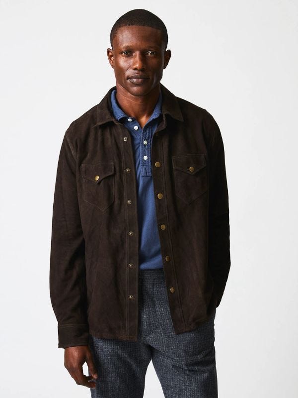 man from the waist up wearing a brown suede workshirt over a navy polo shirt with textured trousers