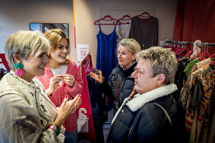 Four women talk in a store with vintage clothing on racks.