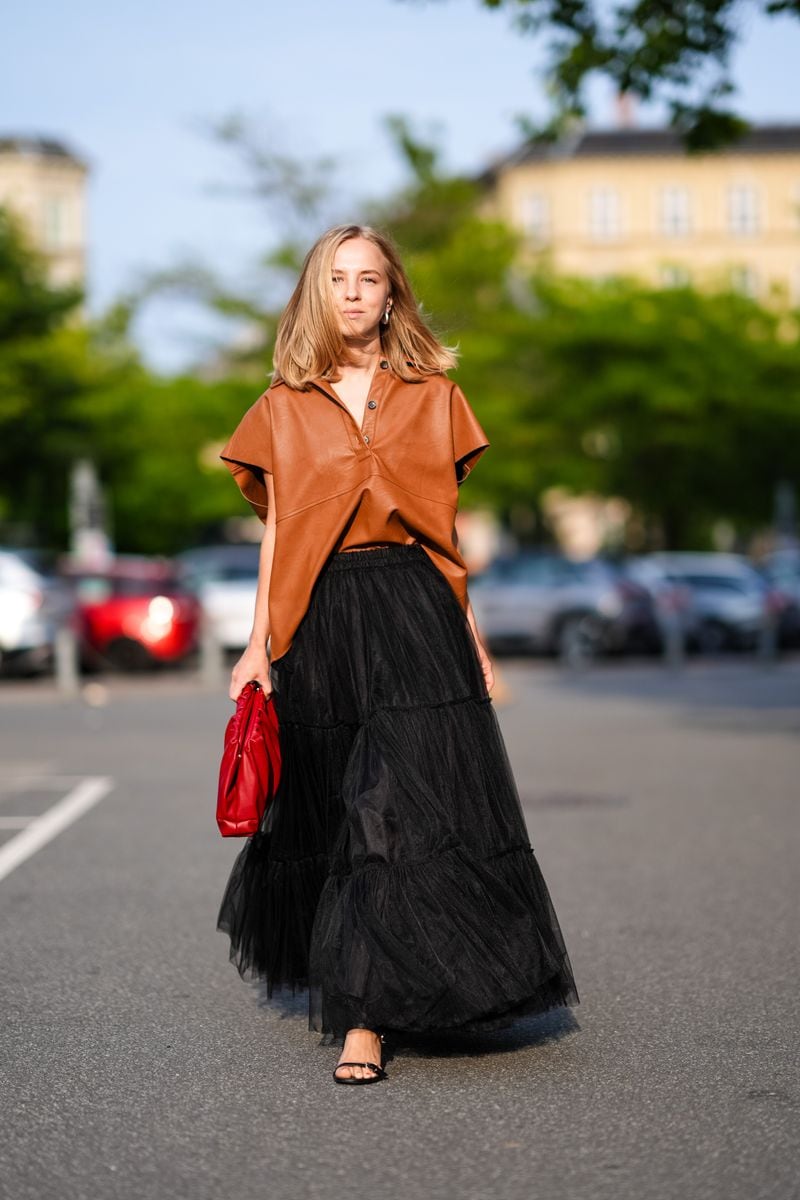 A guest wears gold earrings, shiny light brown short sleeve shirt, bright red leather bag, black sheer mesh maxi skirt, black open toe heels, outside Baum und Pferdgarten, during the Copenhagen Fashion Week Spring/Summer 2024-2025 on August 7, 2024 in Copenhagen, Denmark. (Photo by Edward Berthelot/Getty Images)