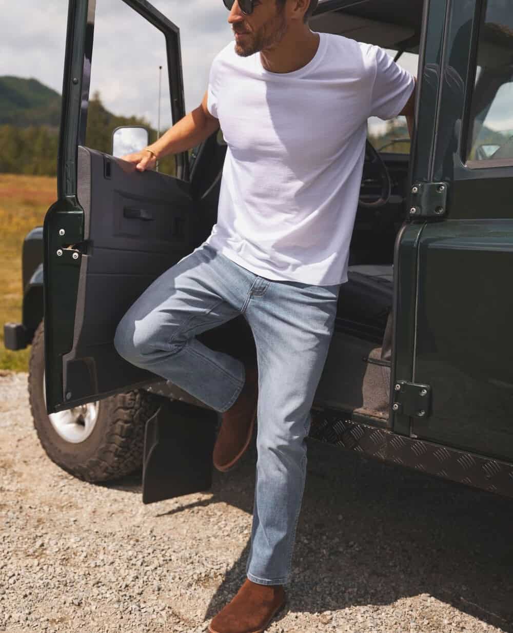 man in a white t-shirt and jeans getting down from a vehicle