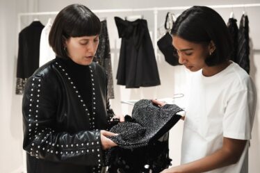 Two designers study a piece of material, with a rack of clothing displayed behind them.