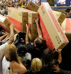 Shoppers crowd together, some holding television boxes above their heads.