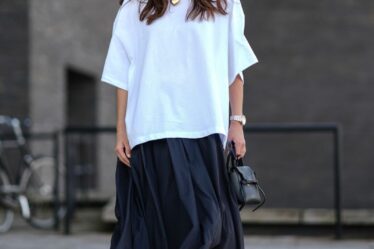 A guest wears light brown rimmed sunglasses, gold chain with gold heart shaped pendant, white oversized t-shirt, a silver watch, black shiny leather bag, black flowy maxi skirt, shiny black Mary Janeâs leather shoes, outside Forza Collective, during the Copenhagen Fashion Week Spring/Summer 2024-2025 on August 5, 2024 in Copenhagen, Denmark. (Photo by Edward Berthelot/Getty Images)