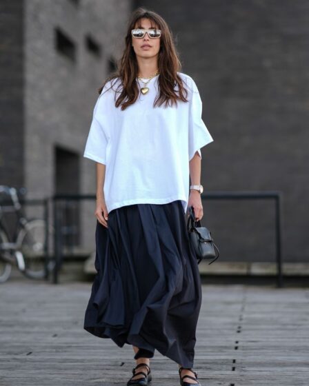 A guest wears light brown rimmed sunglasses, gold chain with gold heart shaped pendant, white oversized t-shirt, a silver watch, black shiny leather bag, black flowy maxi skirt, shiny black Mary Janeâs leather shoes, outside Forza Collective, during the Copenhagen Fashion Week Spring/Summer 2024-2025 on August 5, 2024 in Copenhagen, Denmark. (Photo by Edward Berthelot/Getty Images)