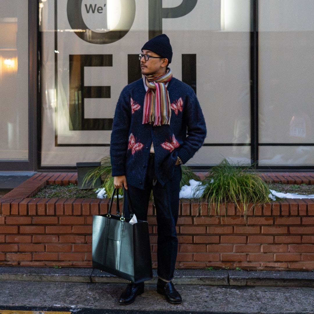 stylish man wearing a bright scarf that coordinates with the pink butterflies on his navy cardigan