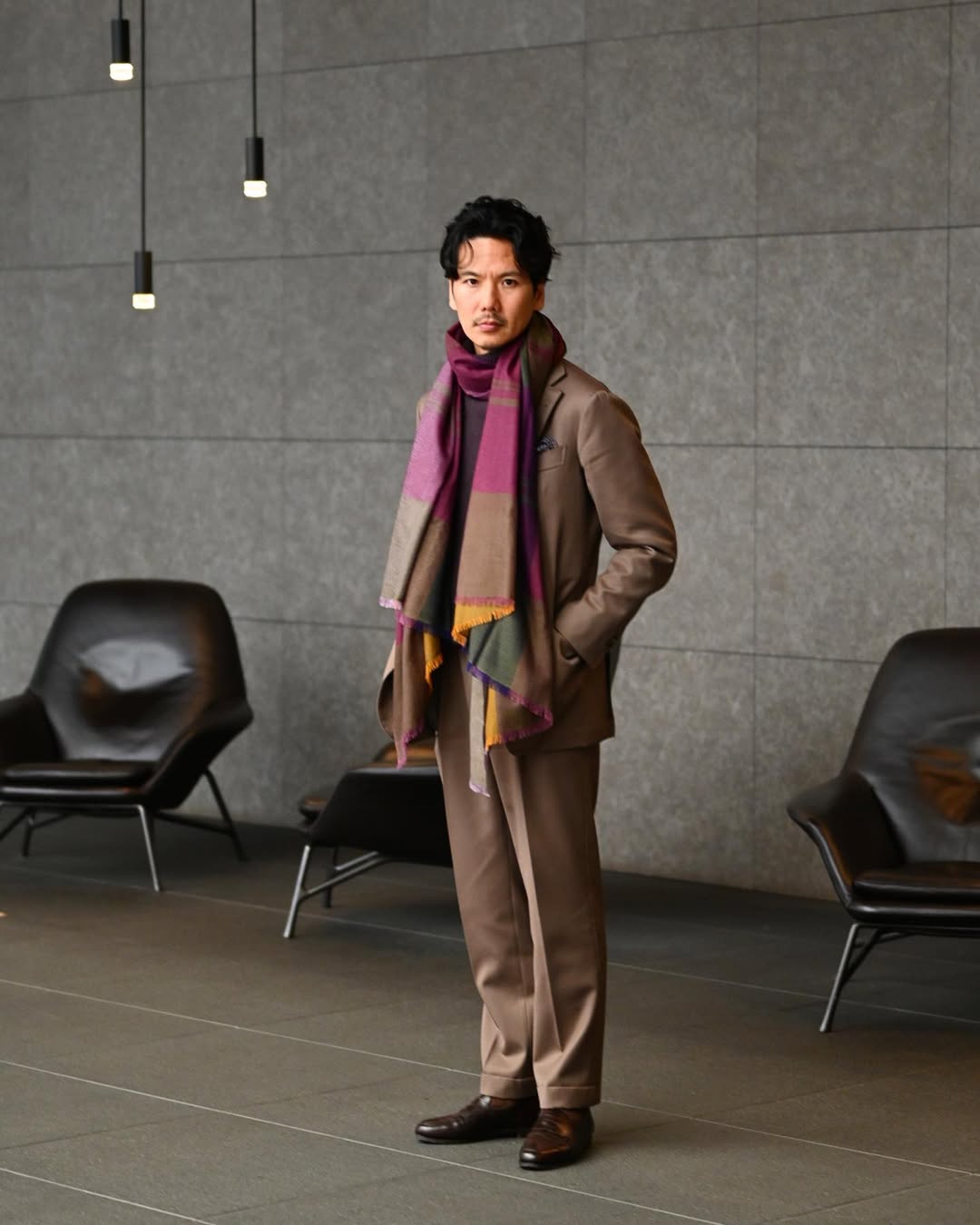 stylish man wearing a brown suit with a large purple patterned silk scarf draped around his neck