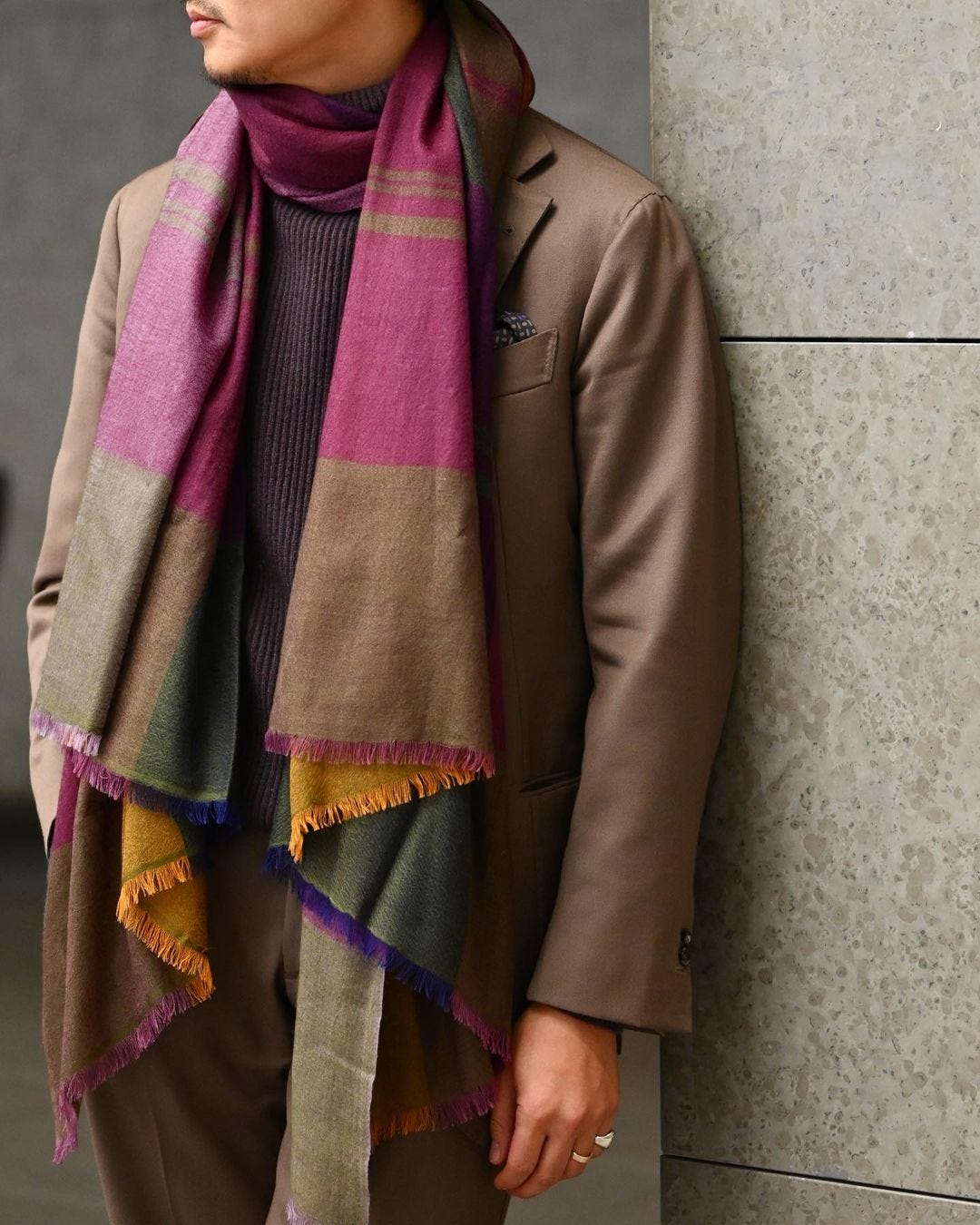 close-up of a stylish man wearing a brown suit with a large purple patterned silk scarf draped around his neck