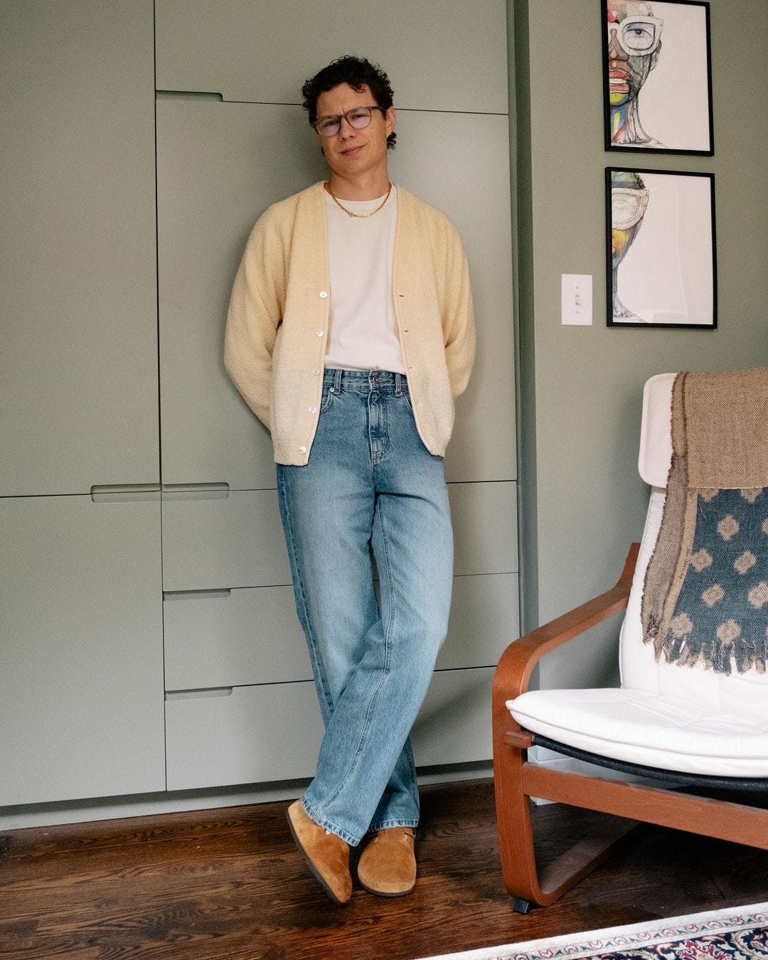 stylish man wearing a cream-colored cardigan over a white t-shirt with light jeans and tan clogs