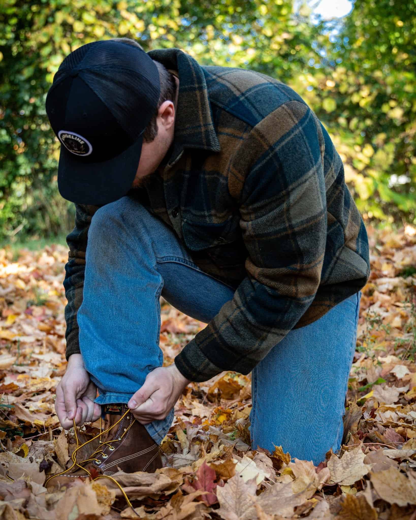 man fixing a shoelace on a ground full of dry leaves