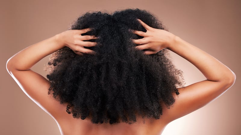 A model has her back to the camera and is running her hands through her curly hair