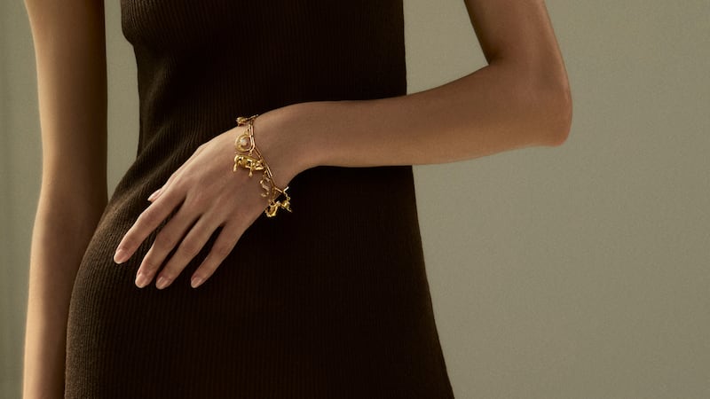 A model wears a gold bracelet with multiple charms.