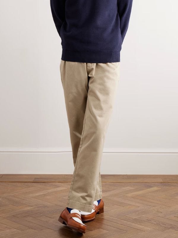 man from the waist down wearing a navy sweater and tan chinos with brown and white loafers