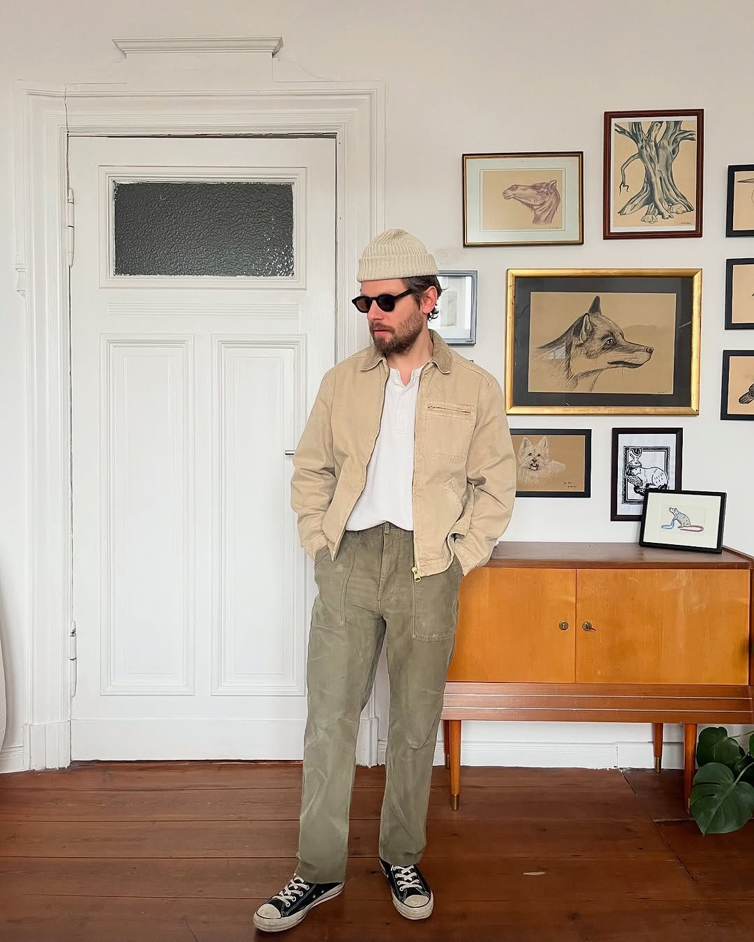 stylish man wearing a tan workwear jacket, white henley, and tan utility pants with converse sneakers