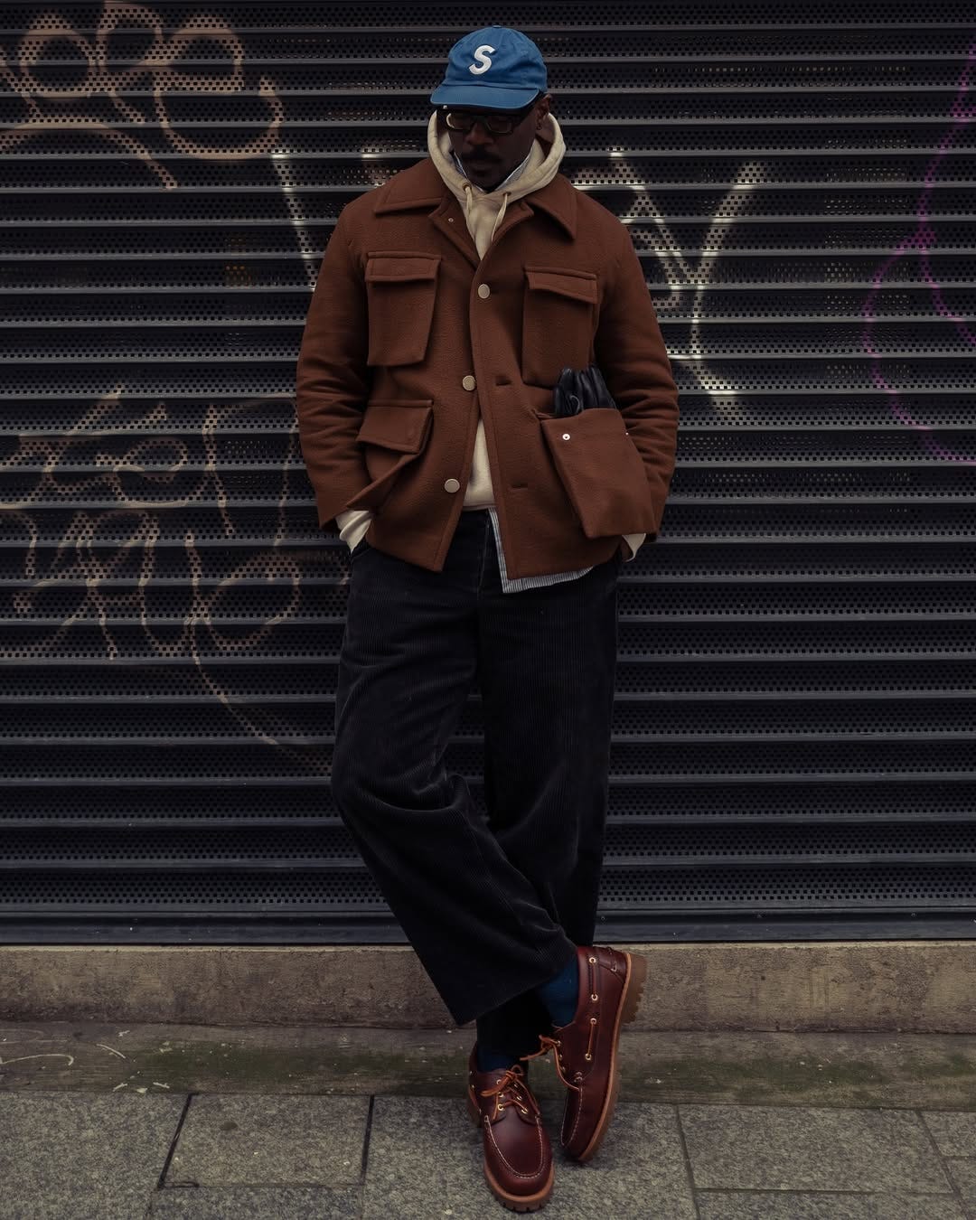 stylish man wearing a brown chore coat with front pockets, tan hoodie, dark corduroy pants and brown shoes