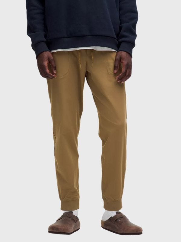 man from the waist down wearing a navy sweatshirt with tan joggers and slip-on brown clogs with white socks