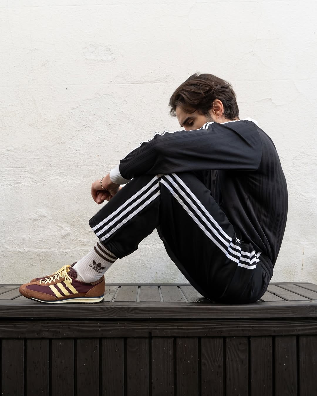 man sitting down wearing a pair of black track pants with white stripes and brown sneakers