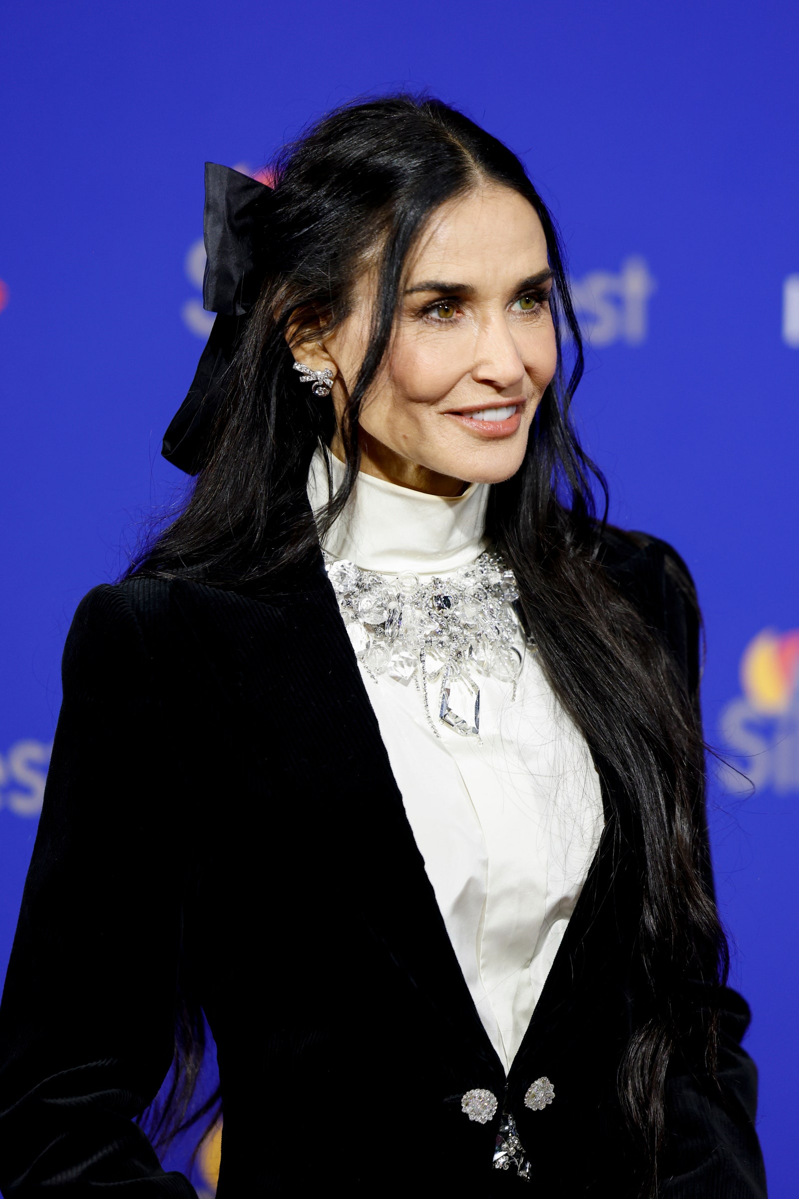 Demi Moore appears at an awards show in a black suit and white shirt. Her hair is pulled half up and cinched with a...