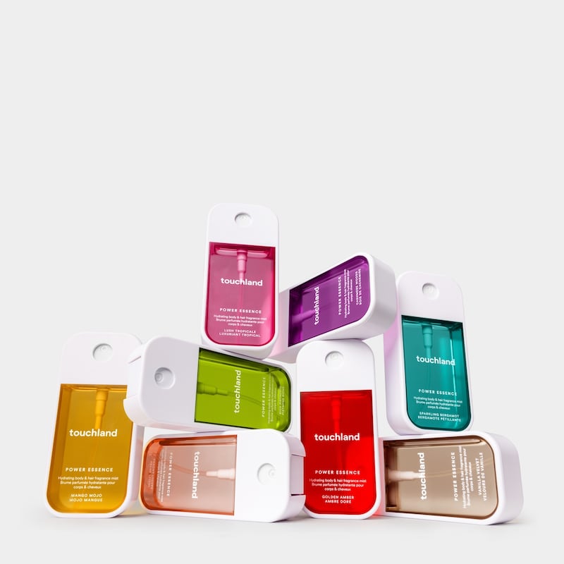 Eight bottles of Touchland's new Power Essence Hair and Body Fragrance Mist are seen on a white background. Their rectangular bottle is white with each featuring a tinted chamber in a candy color.