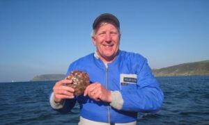 Andy Elliott, who was part of a team who discovered the UK's oldest shipwreck, sitting in a boat at sea, holding a bronze age copper bun ingot